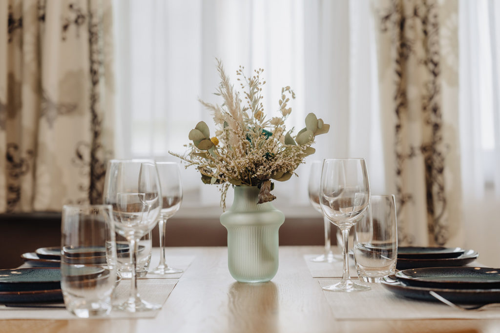 türkisfarbige vase mit trockenblumen auf gedecktem Tisch